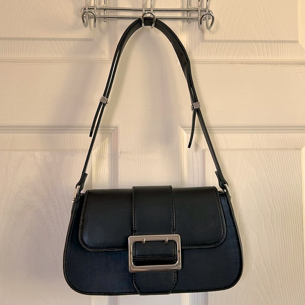 Black Zara baguette bag with a square buckle detail on the front flap, hanging against a white wall